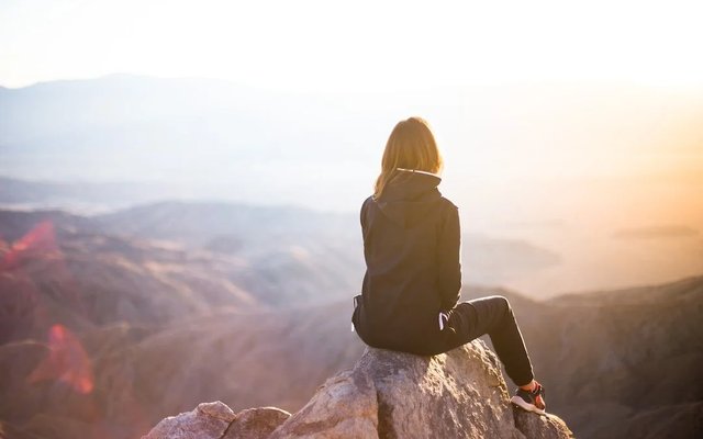 A person standing on a rock at sunset, arms raised