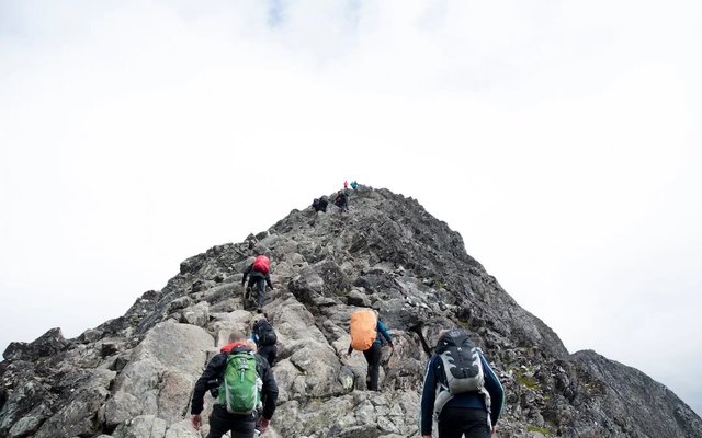 A group celebrating together on a mountain summit at sunset